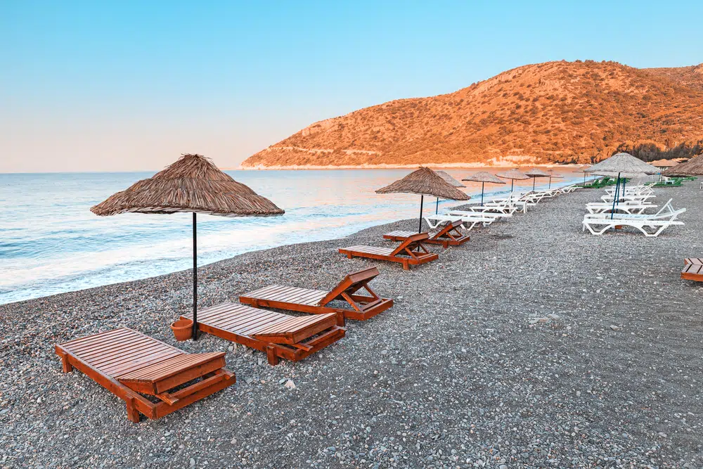 sunbeds and sun umbrellas await vacationers on the shingle beach at ovabuku beach on the datca peninsula in turkey. the photo was taken in the early morning at sunrise